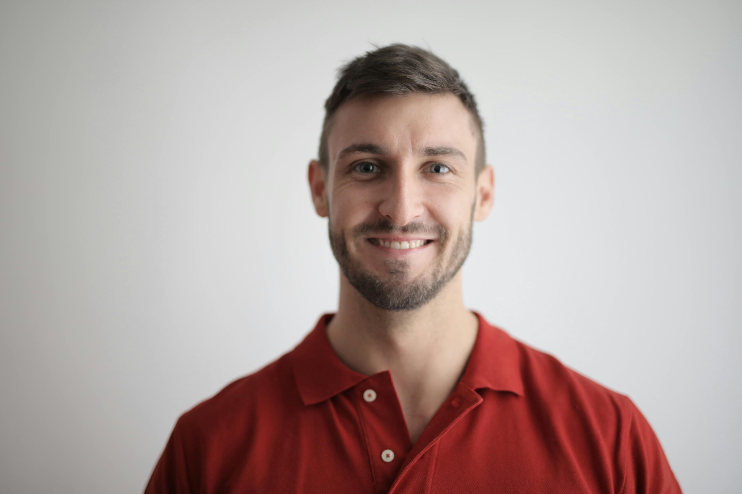 Headshot of a happy man with a beard wearing a red polo shirt against a white background.