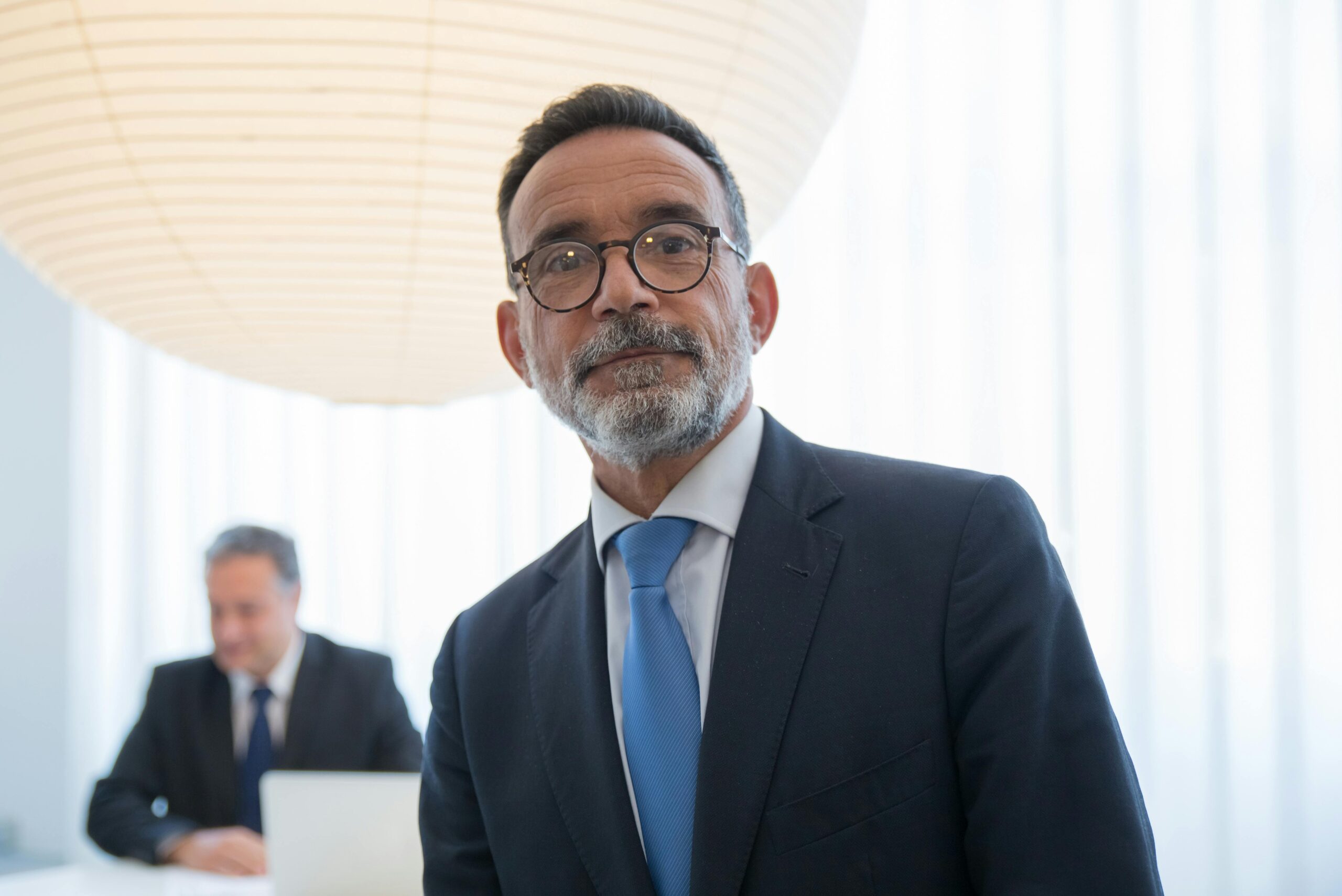 Confident senior executive in formal attire with modern office background.